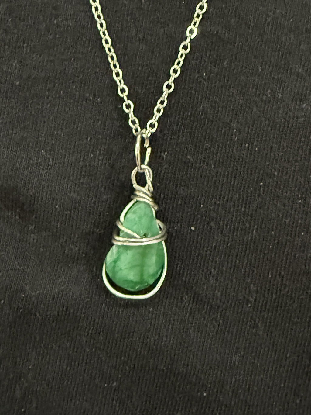 Close-up of green teardrop-shaped emerald stone with decorative wire wrapping
