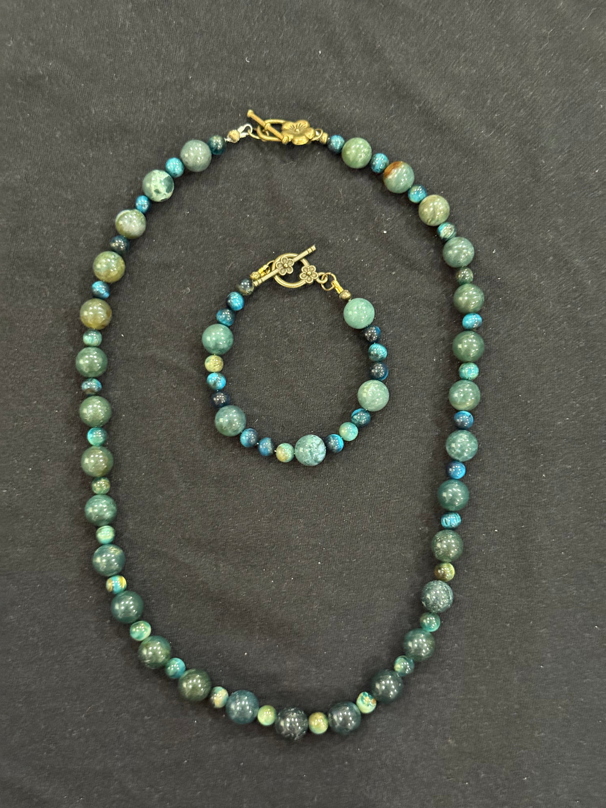 Matching beaded necklace and bracelet in green and teal shades with gold-tone toggle clasps.